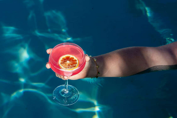 Hand holding pink cocktail with dehydrated citrus slice garnish in pool, premium dried citrus garnishes Australia